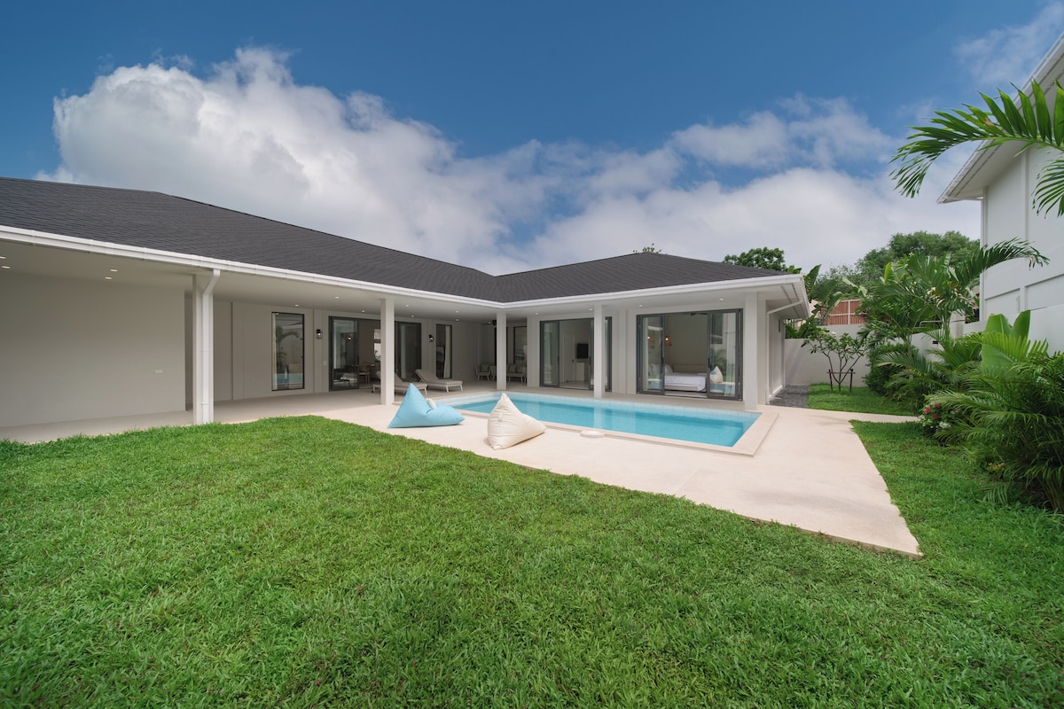 A modern house with a swimming pool, covered patio, and lush green lawn.