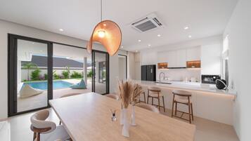 A modern kitchen with a central island, a dining area with a table and chairs, and a view of a swimming pool outside.