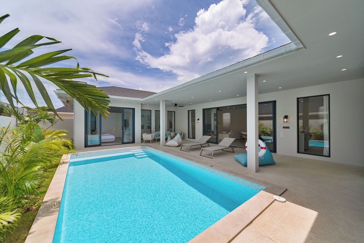 A modern poolside area with a clear blue pool, lounge chairs, and a covered seating area.