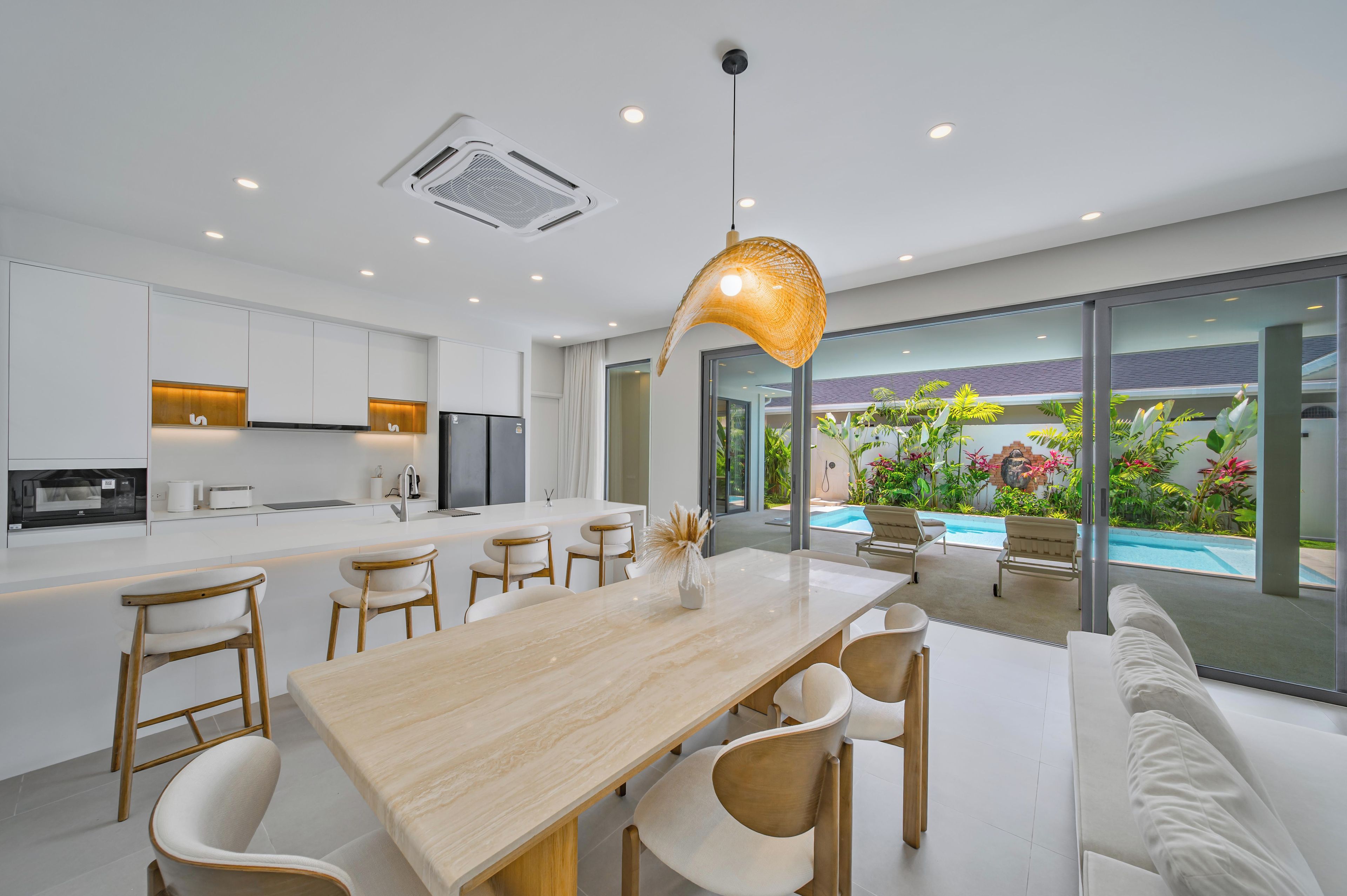 A modern kitchen with a central island, dining area with chairs, and a view of a swimming pool.