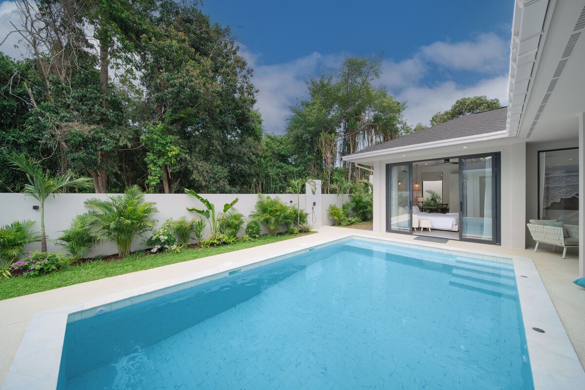 A modern poolside area with a clear blue pool, a glass-enclosed patio, and lush greenery.