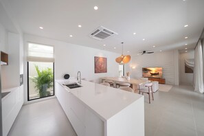 Una cocina moderna con una isla central, un comedor con mesa y sillas, y un ventanal con vistas a zonas verdes.