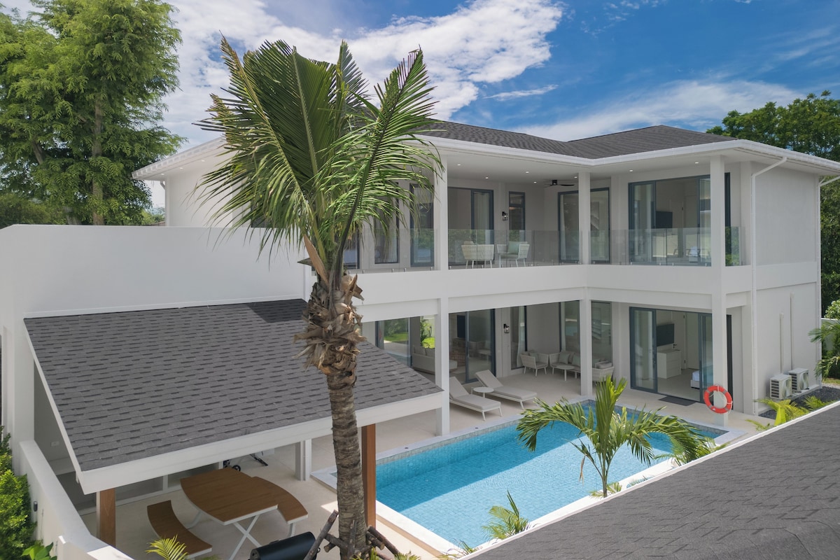 A modern two-story house with a swimming pool, outdoor seating, and a palm tree.