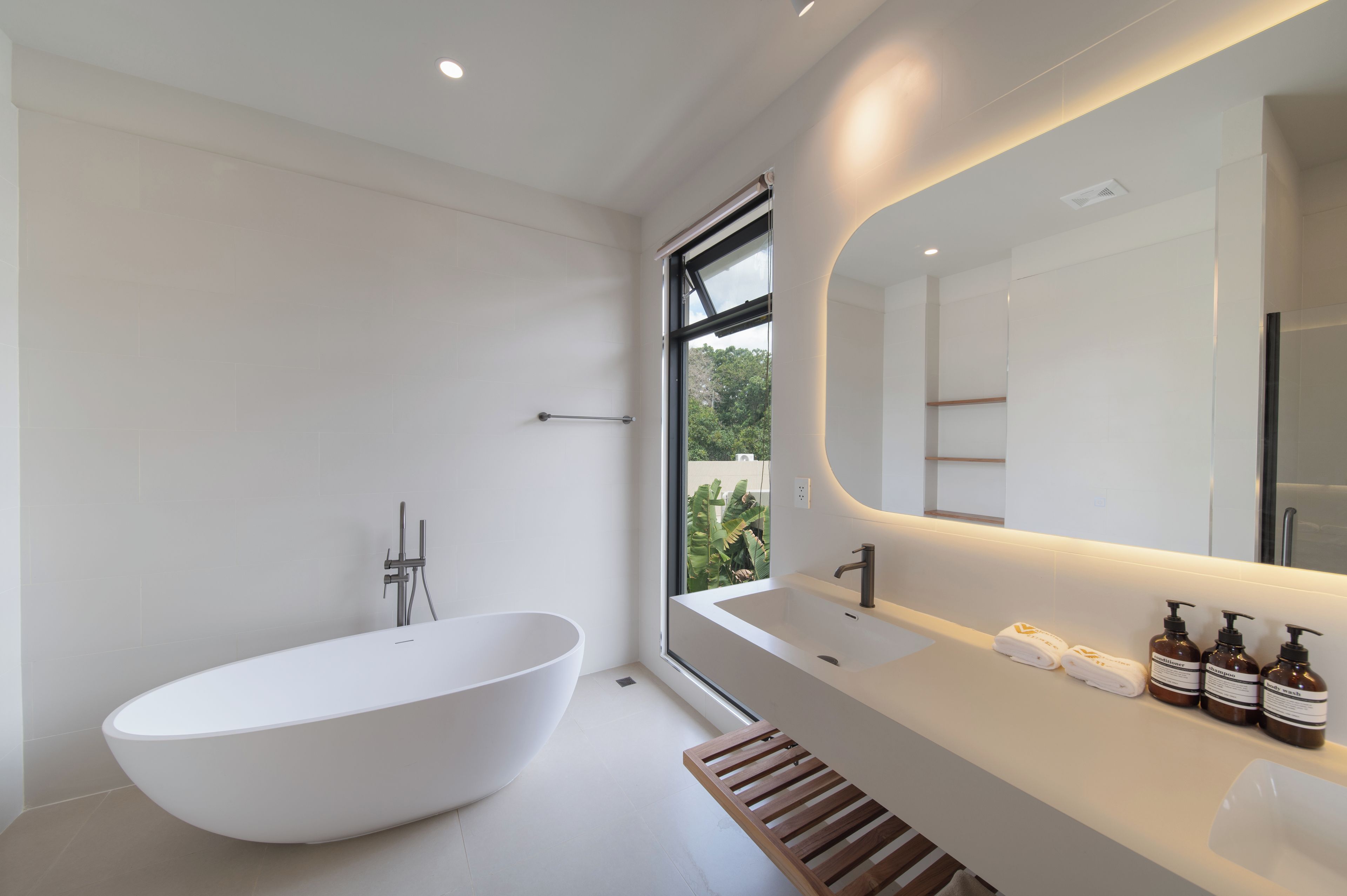 Un baño moderno con una bañera independiente, un espejo grande y una ventana que ofrece vistas a la vegetación.
