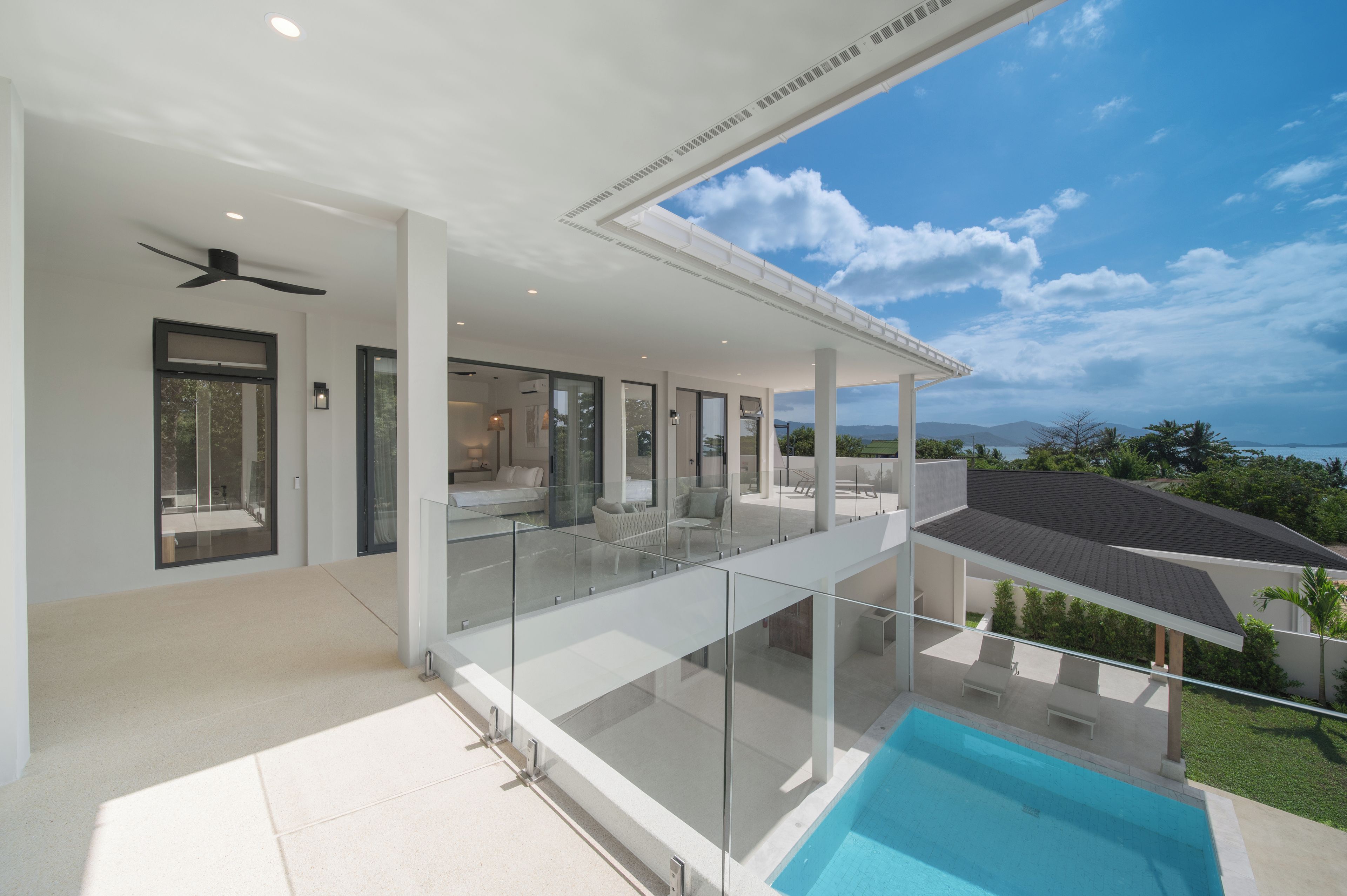 A modern house with a glass balcony overlooking a swimming pool and a clear sky.