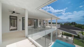 A modern house with a glass balcony overlooking a swimming pool and a clear sky.