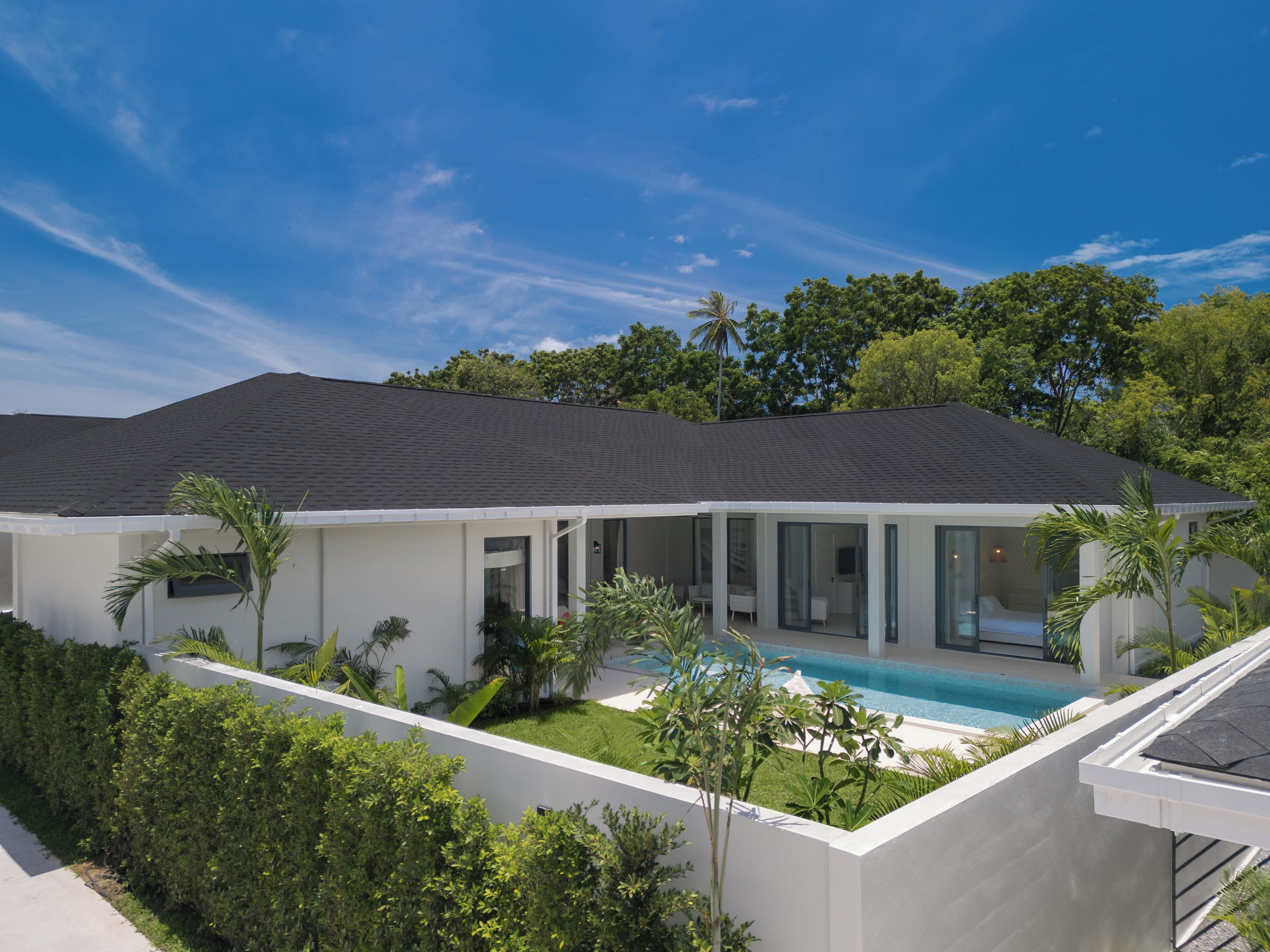 A modern house with a swimming pool, surrounded by lush greenery and a clear blue sky.