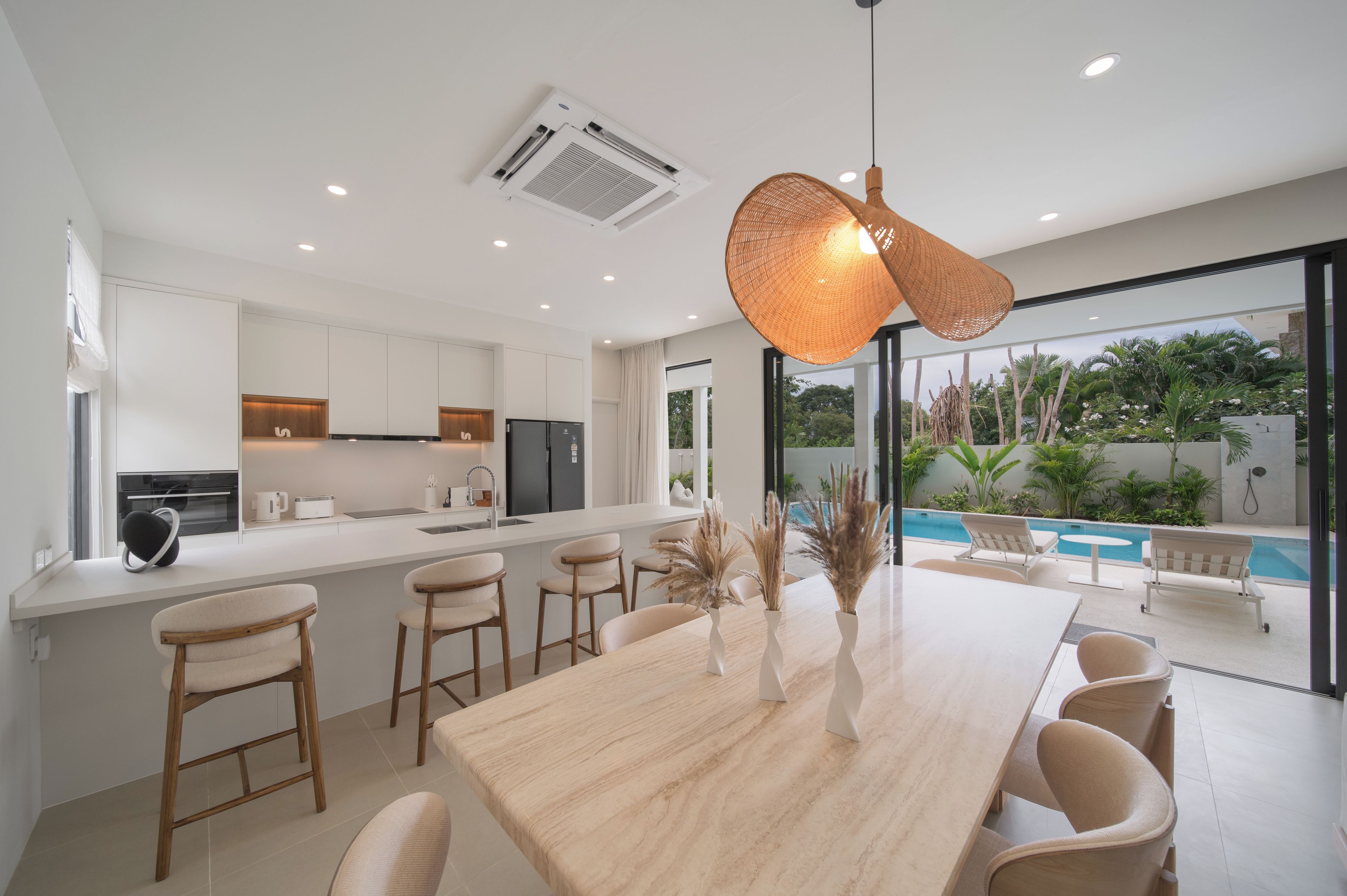 A modern kitchen with a central island, a dining area with a large table and chairs, and a view of a swimming pool through large windows.