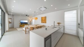 A modern kitchen with a large island, dining area, and a TV in the background. - Valentine Village (Koh Samui)