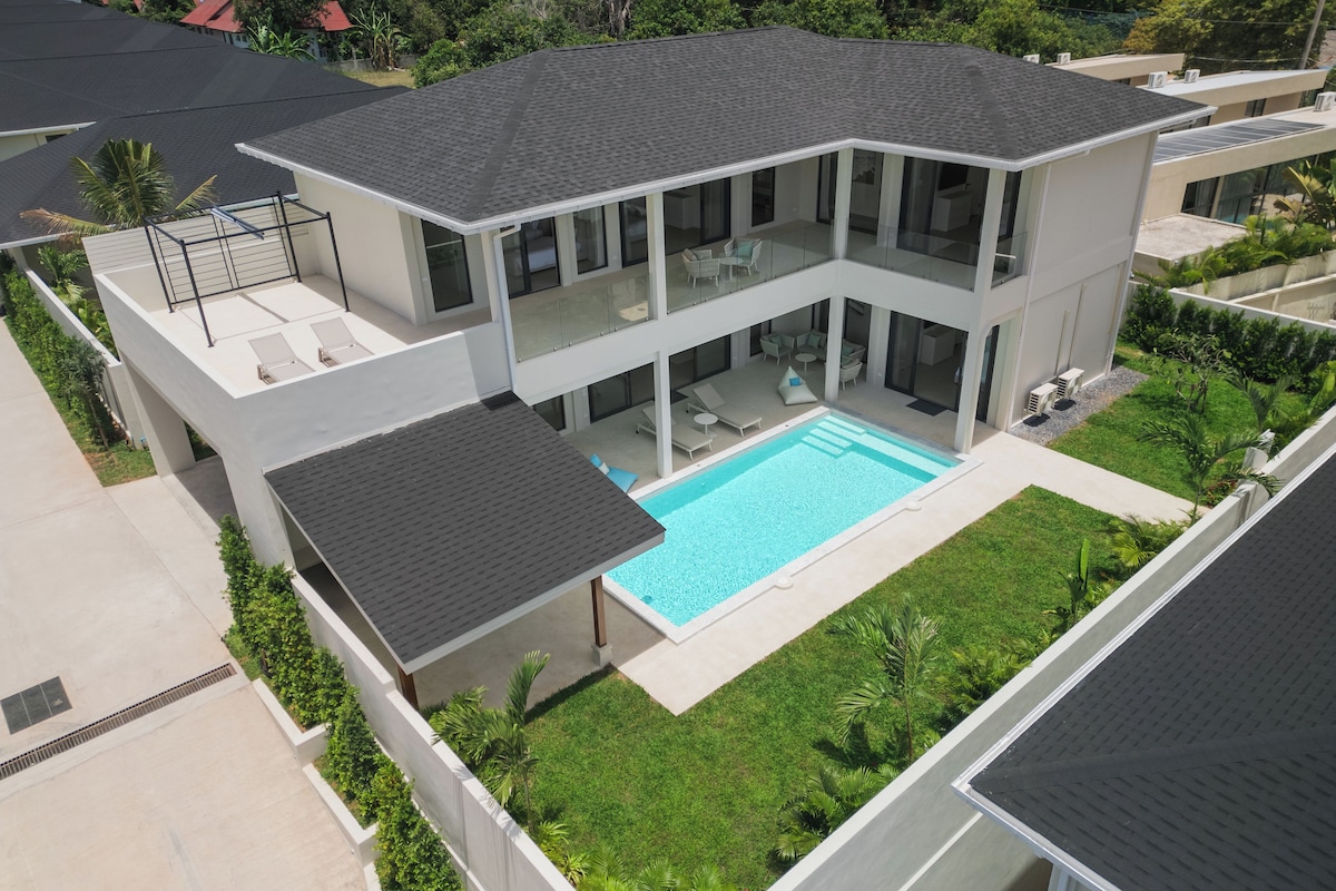 A modern two-story house with a swimming pool, large windows, and a flat roof.