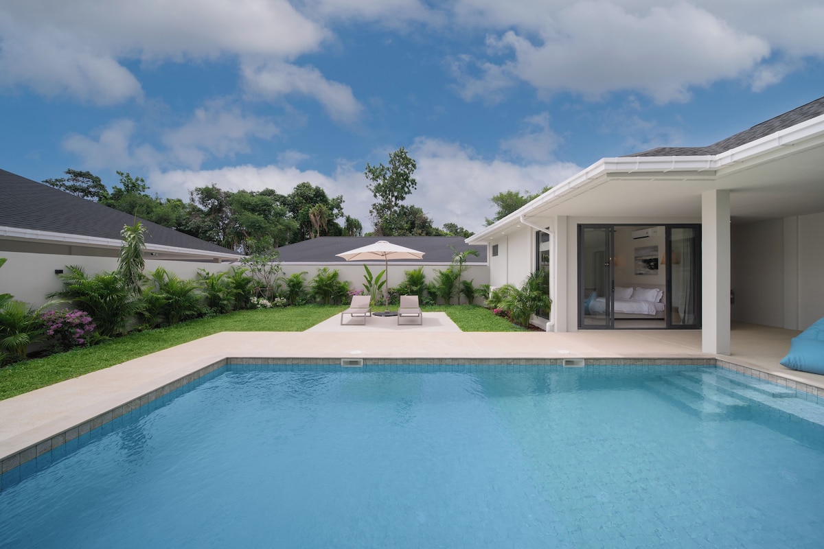 A swimming pool with a clear blue water surface, surrounded by a well-maintained lawn and various plants.