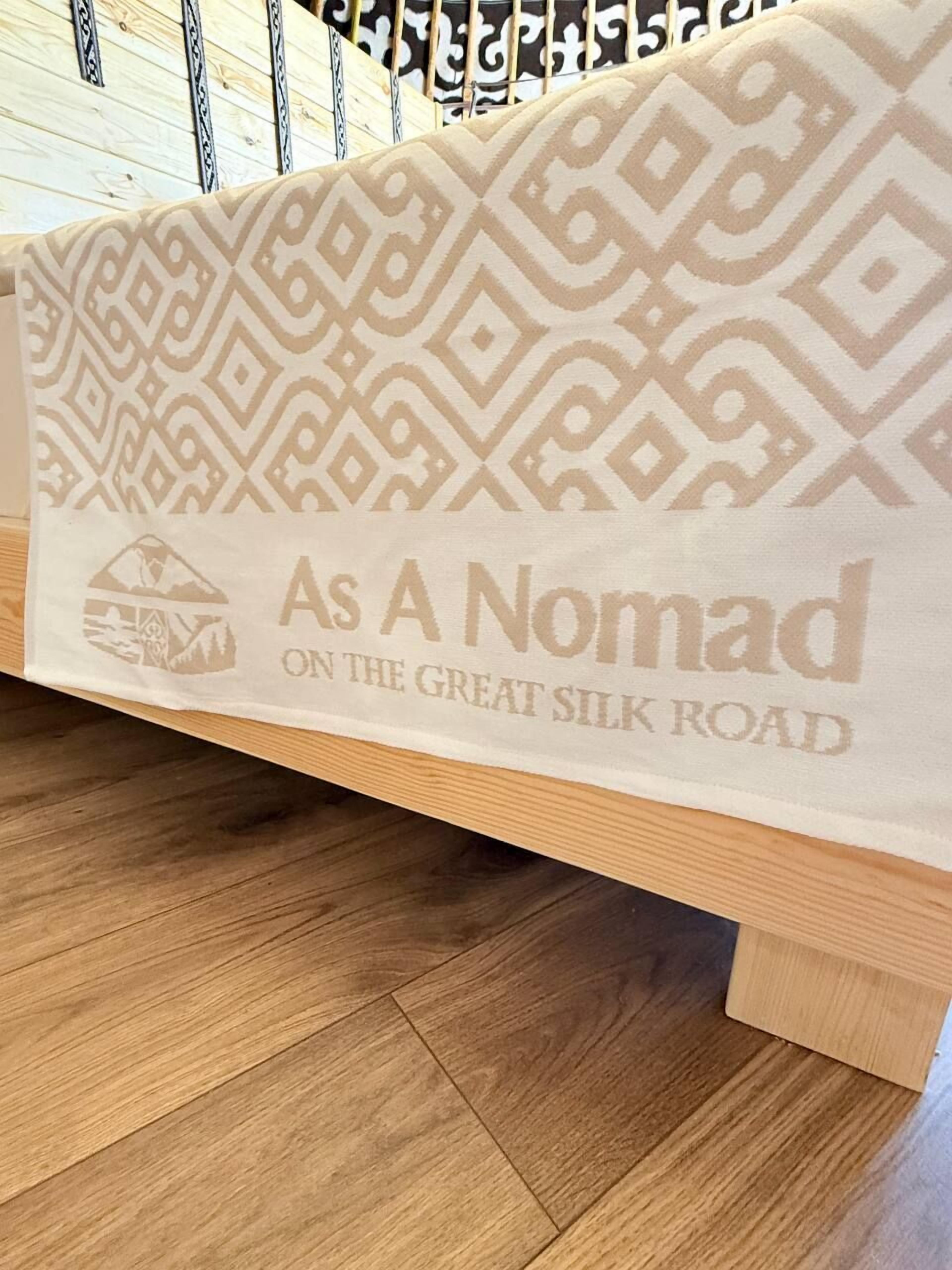 A bed with a patterned blanket and a logo that reads 'As A Nomad ON THE GREAT SILK ROAD'.