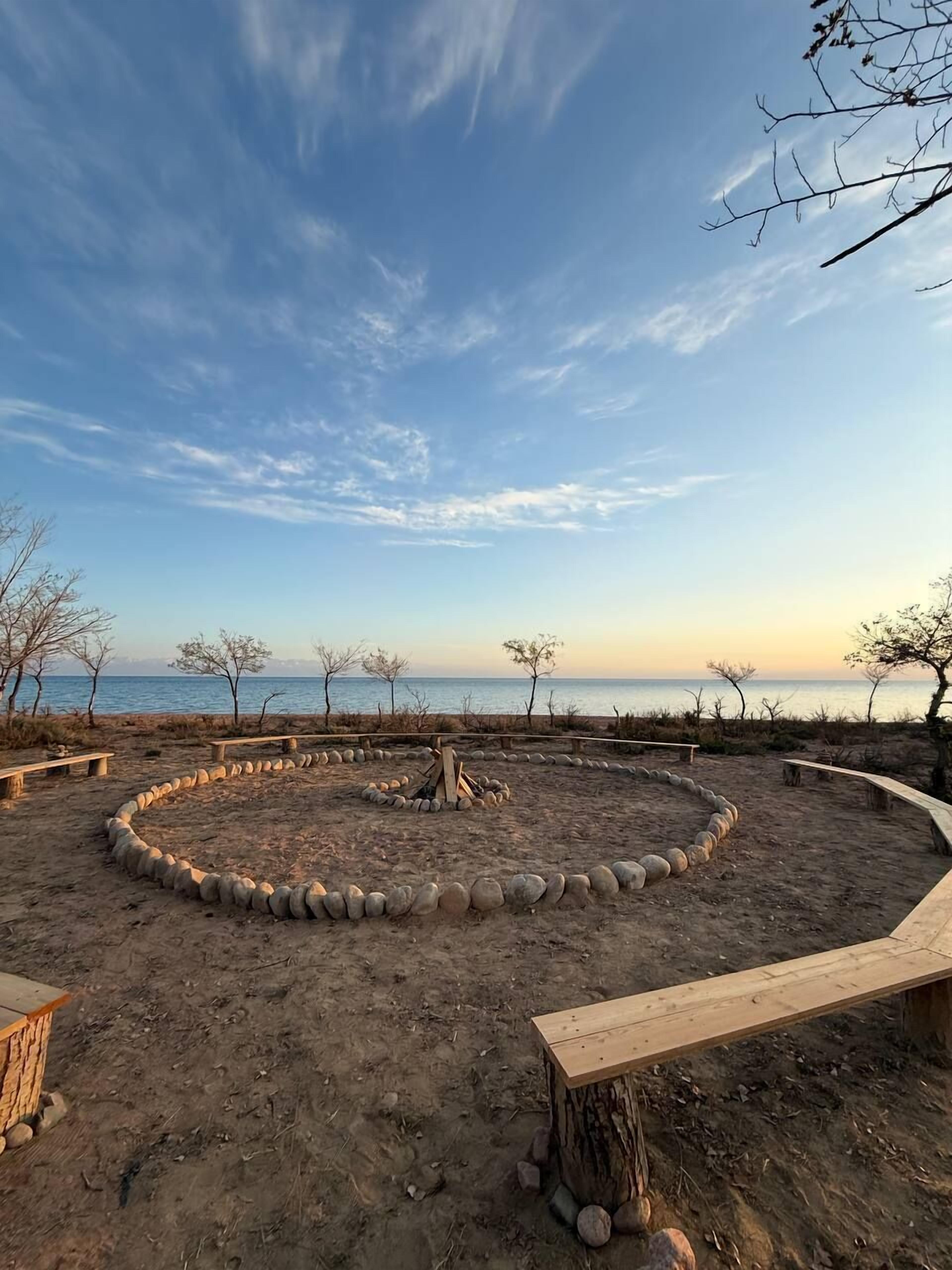 A circular stone fire pit surrounded by benches, with a view of the sea and clear sky.