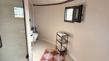 Uma casa de banho com cabine de duche em vidro, lavatório, sanita, um pequeno armário e chão estampado.