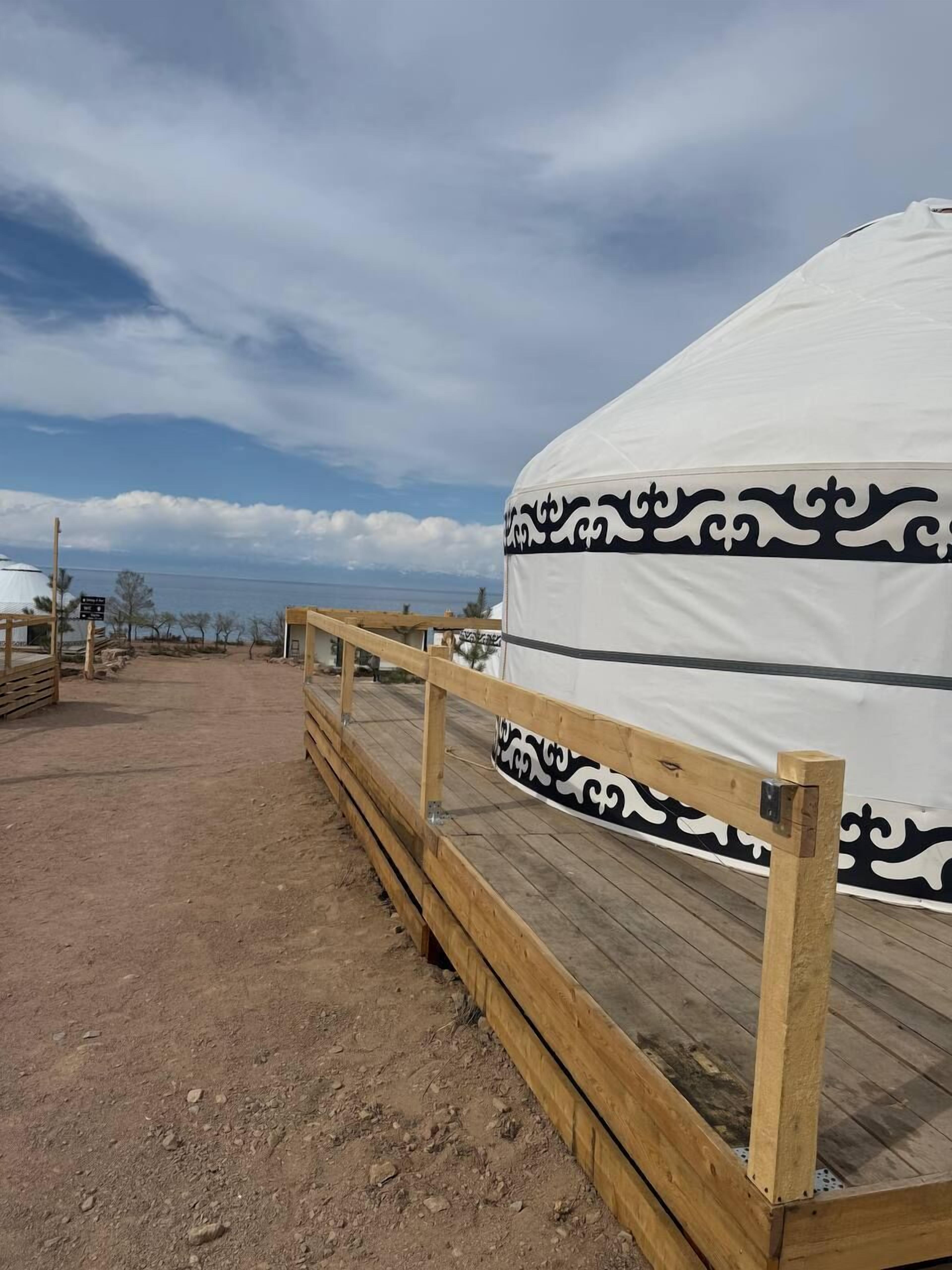 A large white tent with black decorative patterns, a wooden deck, and a clear sky.