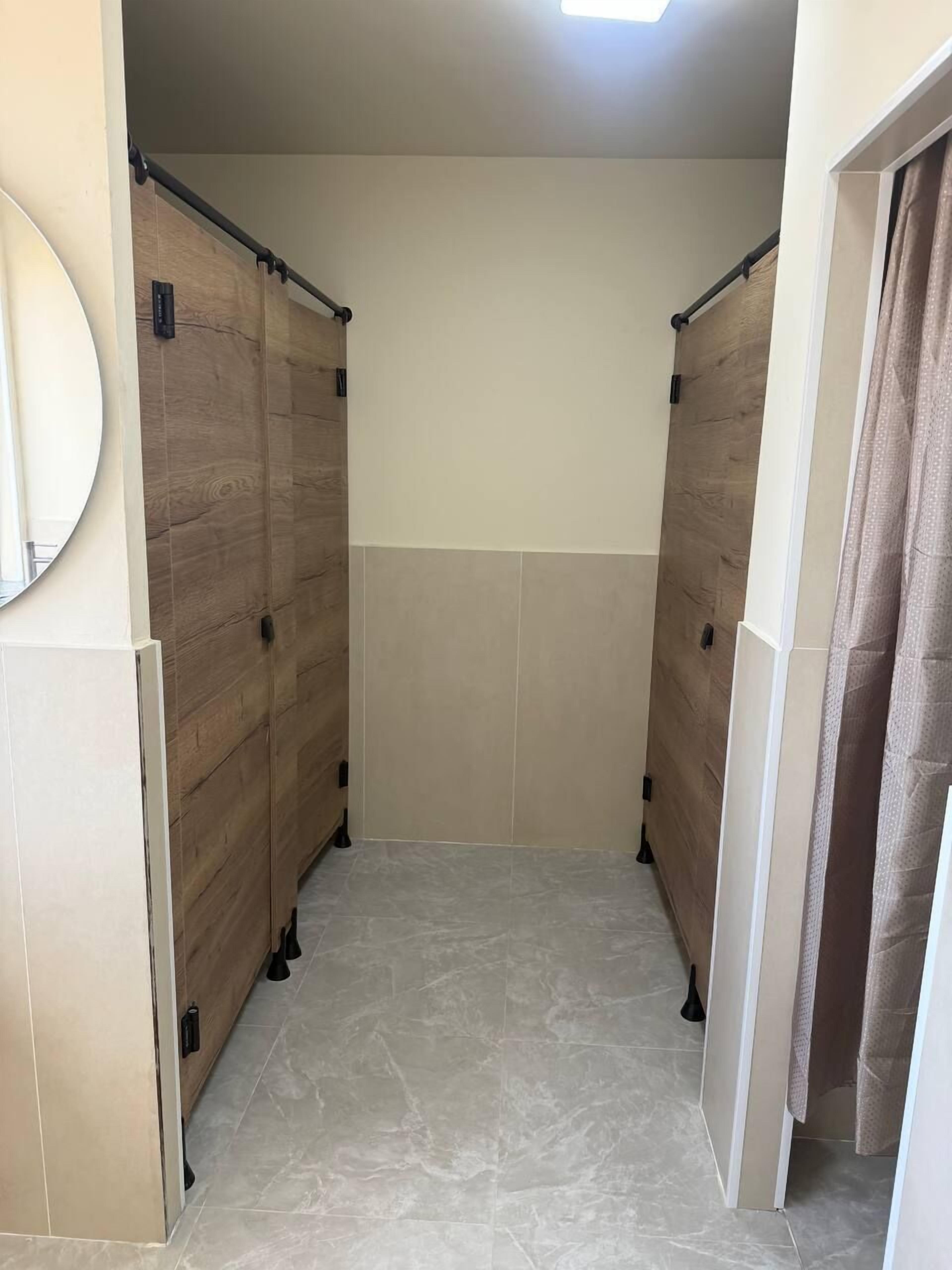 A public restroom with wooden partitions, a mirror, and tiled flooring.
