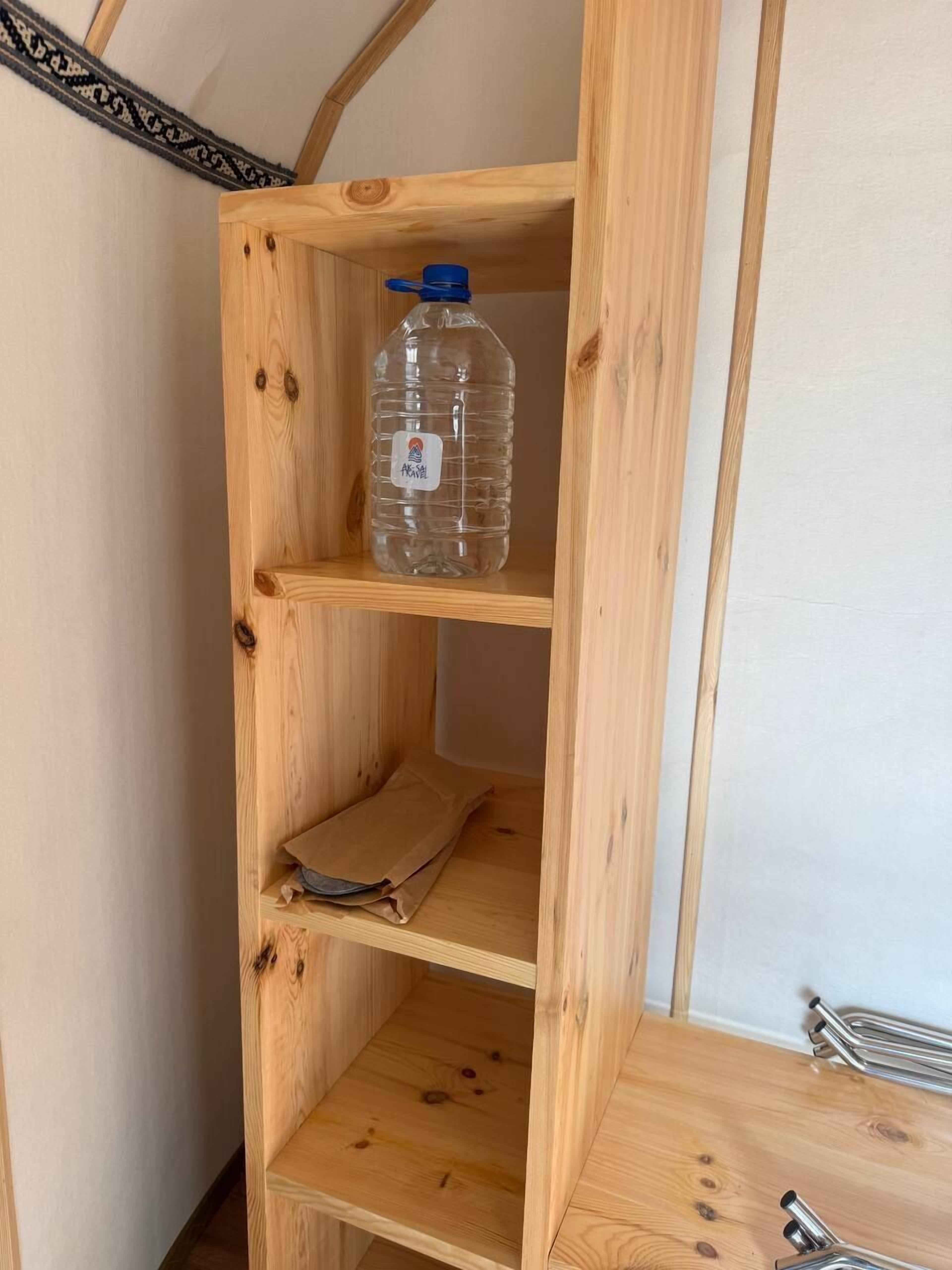 A wooden shelf unit with a water bottle and a folded brown paper item.