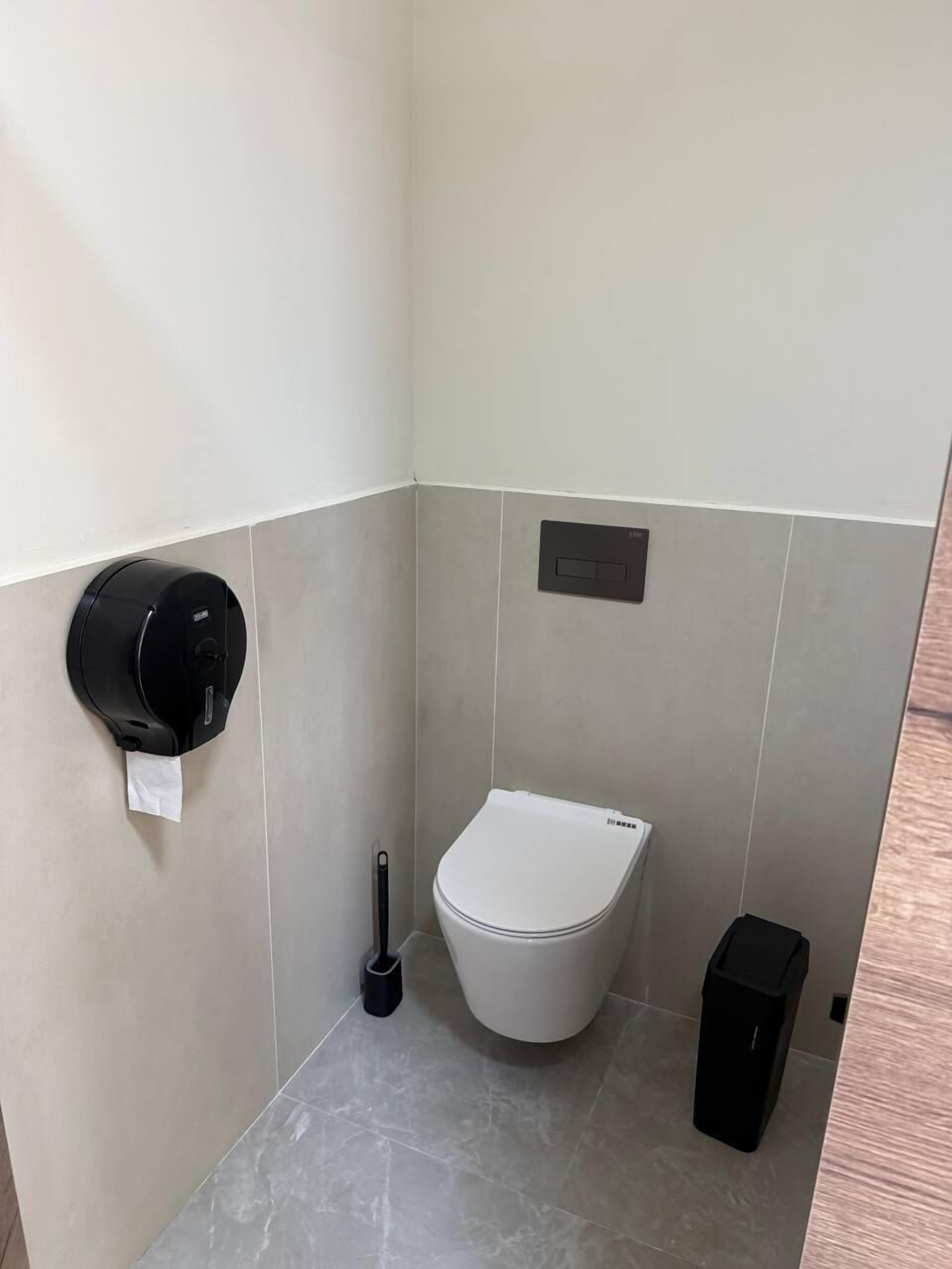 A small, modern bathroom with a toilet, a trash bin, and a paper towel dispenser.