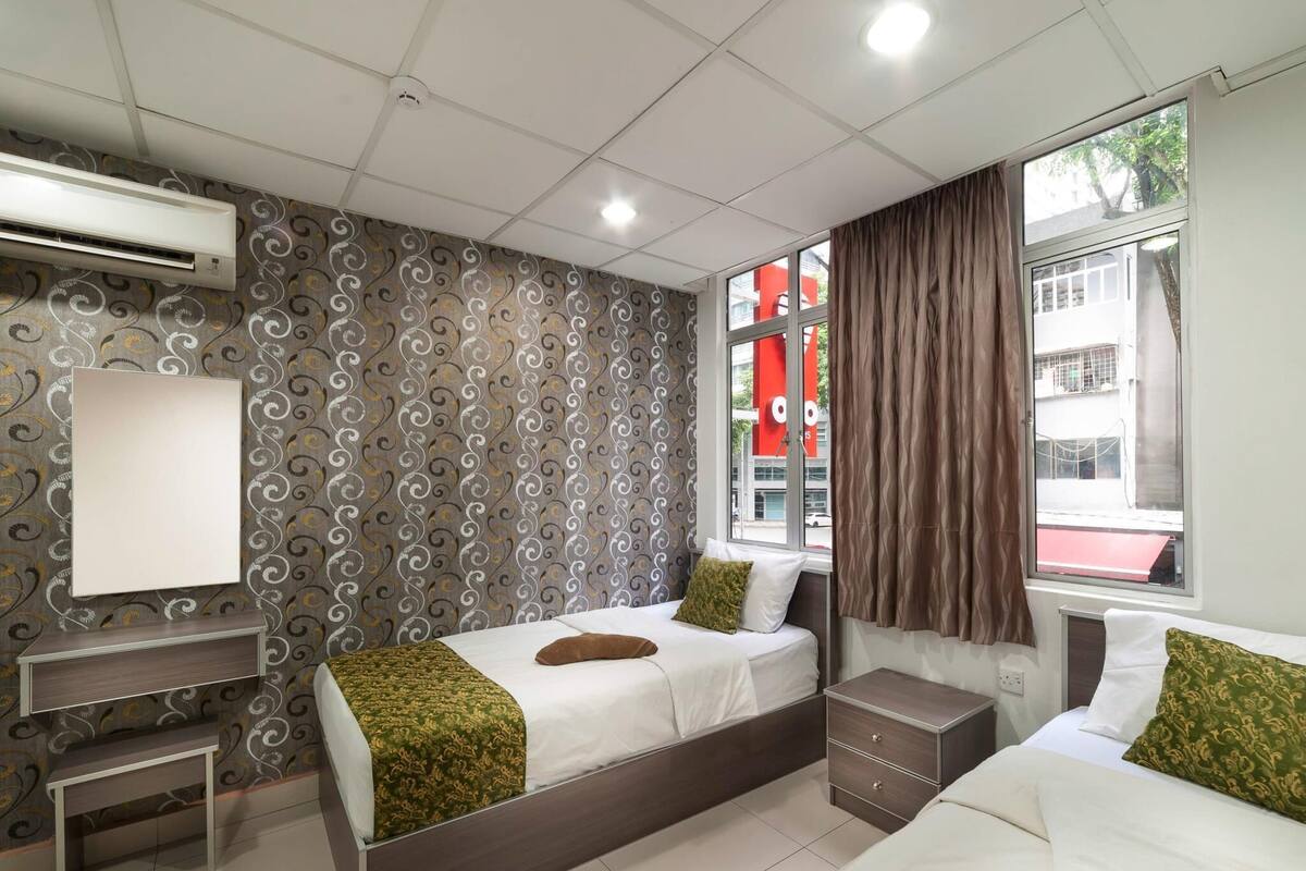 Hotellihuone, jossa on kaksi sänkyä, työpöytä ja suuri ikkuna, jossa on verhot.