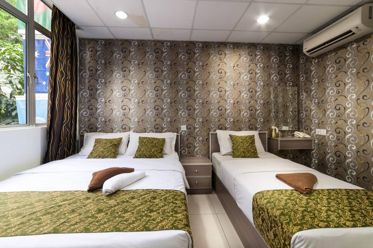 Hotellihuone, jossa on kaksi sänkyä, ikkuna verhoilla, kuvioitu seinä ja ilmastointilaite.
