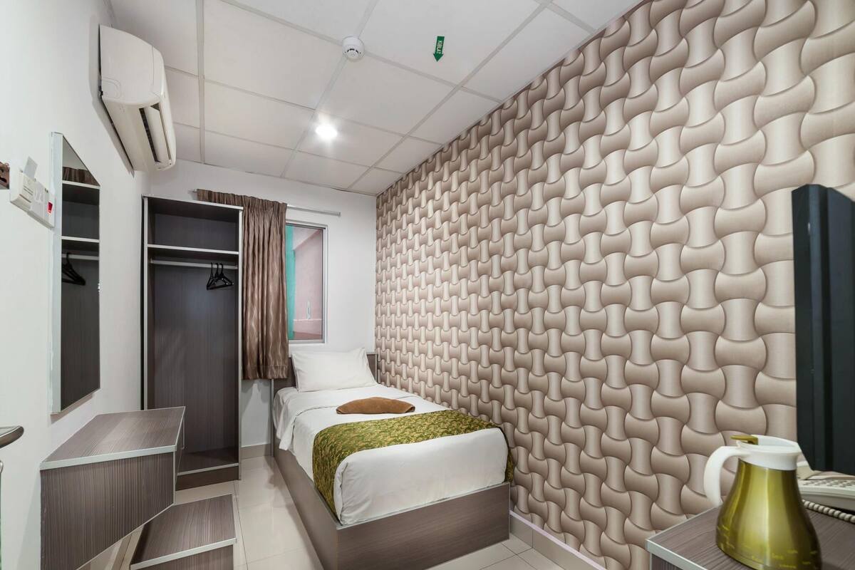 Moderni hotellihuone, jossa on sänky, vaatekaappi, peilillä varustettu meikkipöytä ja kuvioitu seinä.