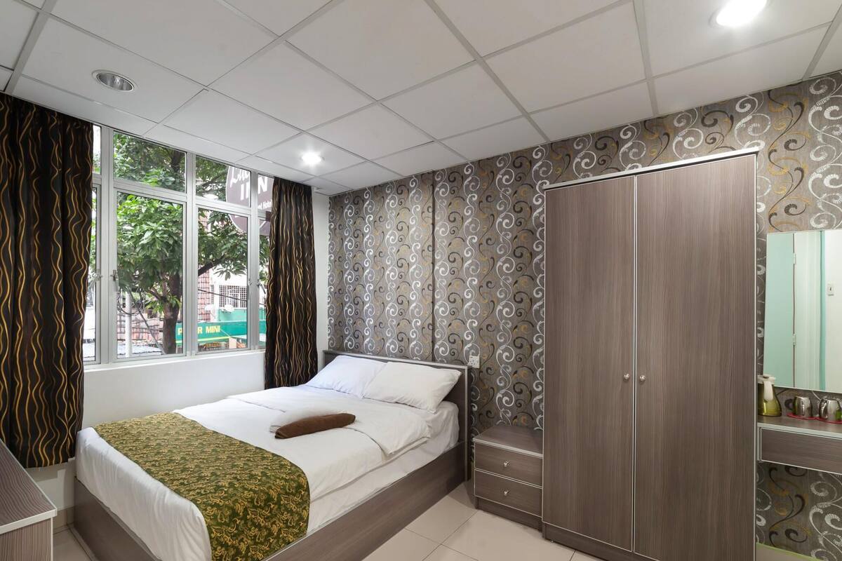 Hotellihuone, jossa on sänky, vaatekaappi, peilillä varustettu meikkipöytä ja ikkuna, jossa on verhot.