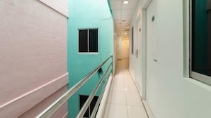 A narrow corridor with a teal and white wall, a metal railing, and a tiled floor. - Lacomme Inn (Kuala Lumpur)