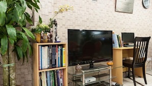 A living room with a flat-screen TV, a bookshelf with books, a potted plant, and a wall clock. - Lacomme Inn (Kuala Lumpur)