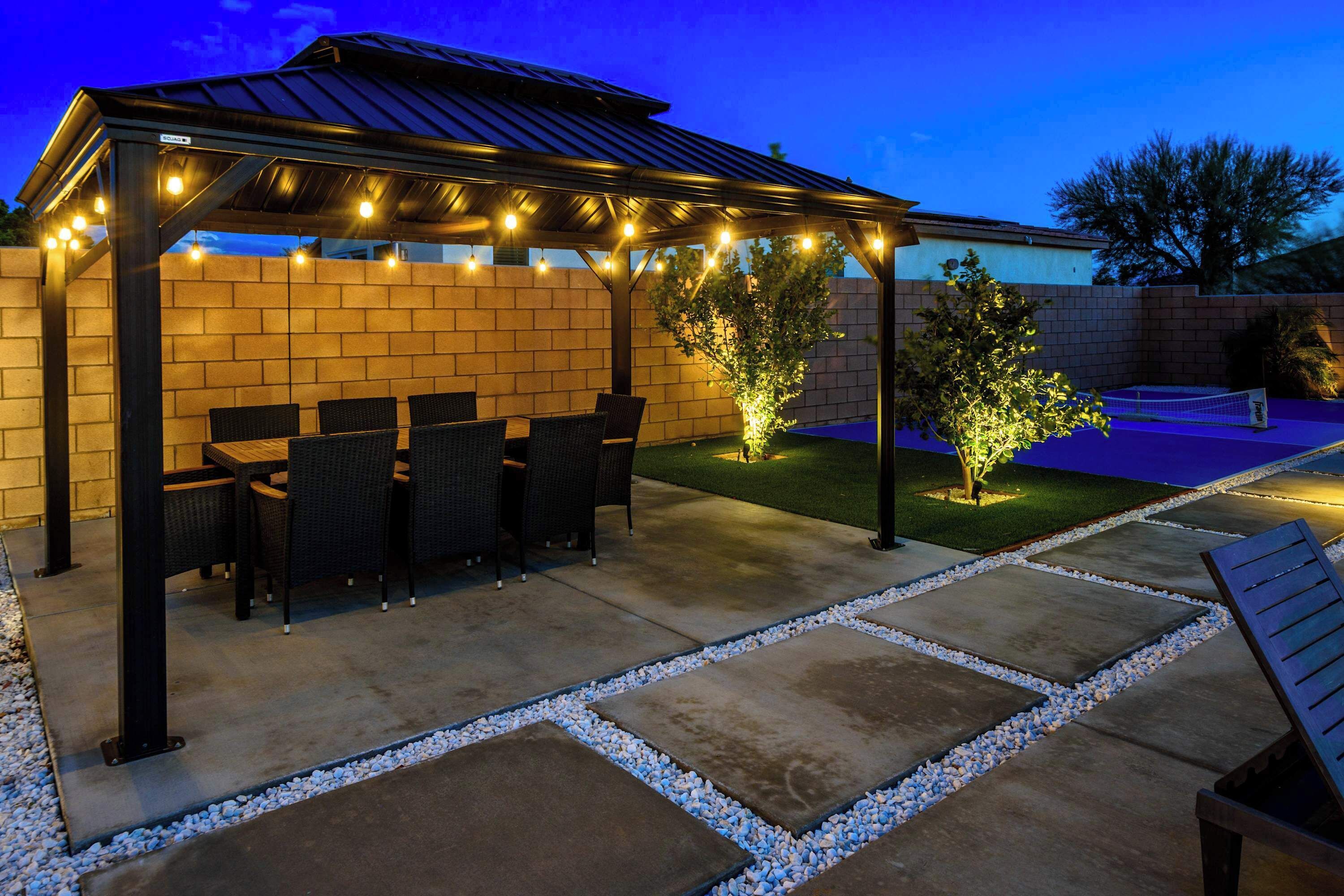 An outdoor patio with a covered seating area, a small lawn, and a tennis court.