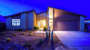 A modern two-story house with a garage, a well-maintained garden with cacti and shrubs, and a driveway leading to the entrance.