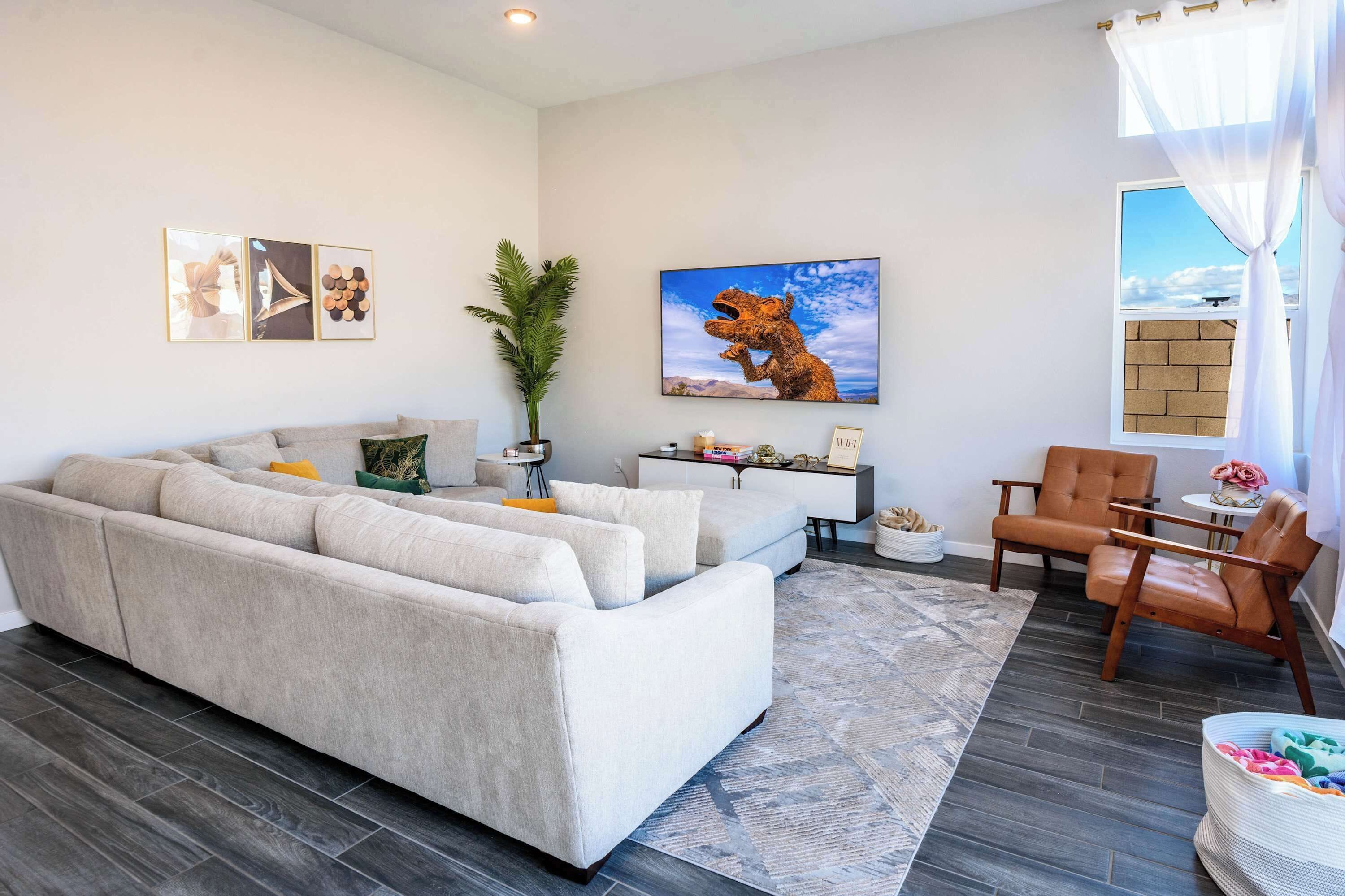 A modern living room with a large sectional sofa, a small side table, a potted plant, and a framed picture on the wall.