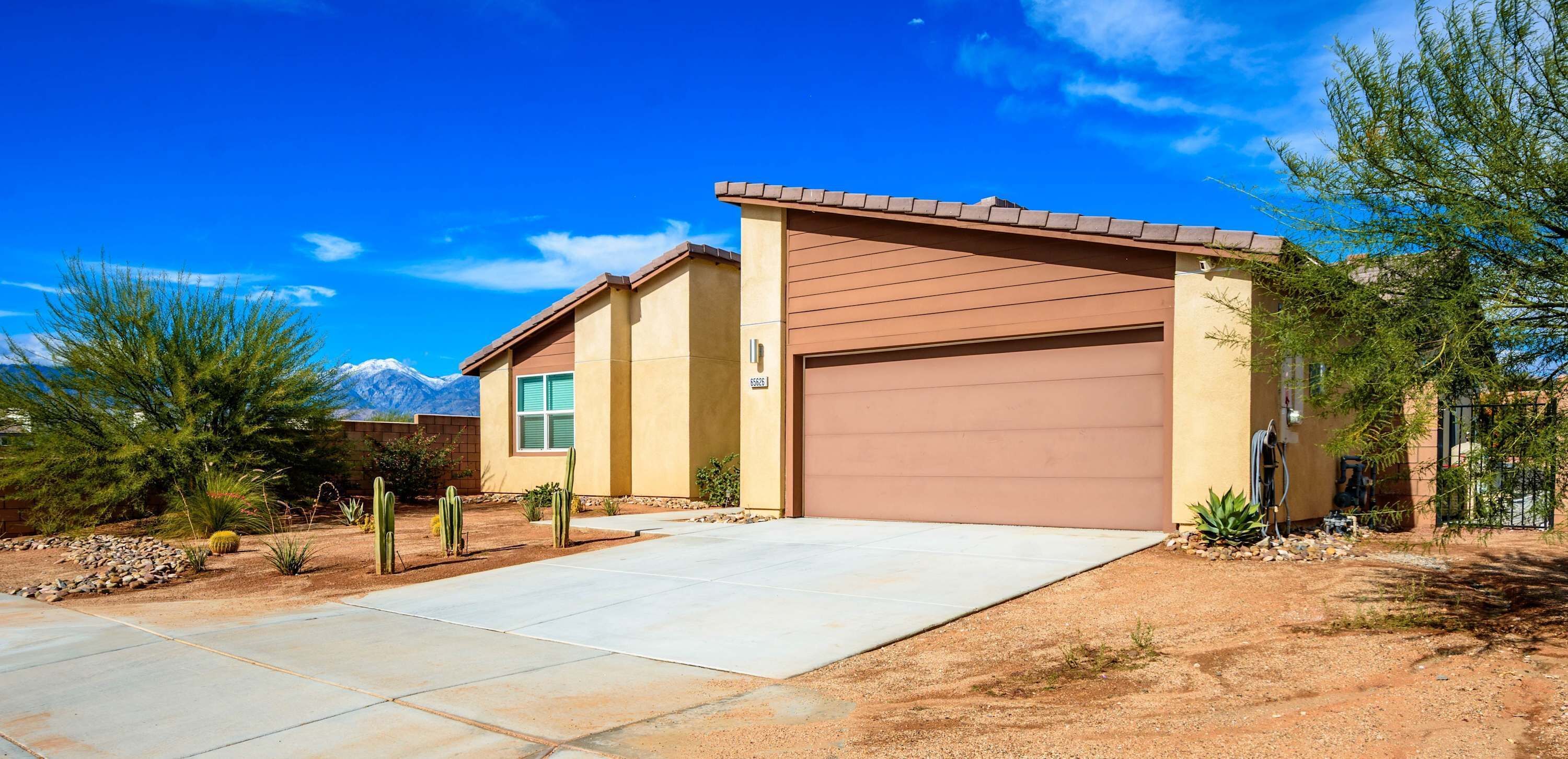 A two-story house with a garage, surrounded by desert vegetation and a clear blue sky.
