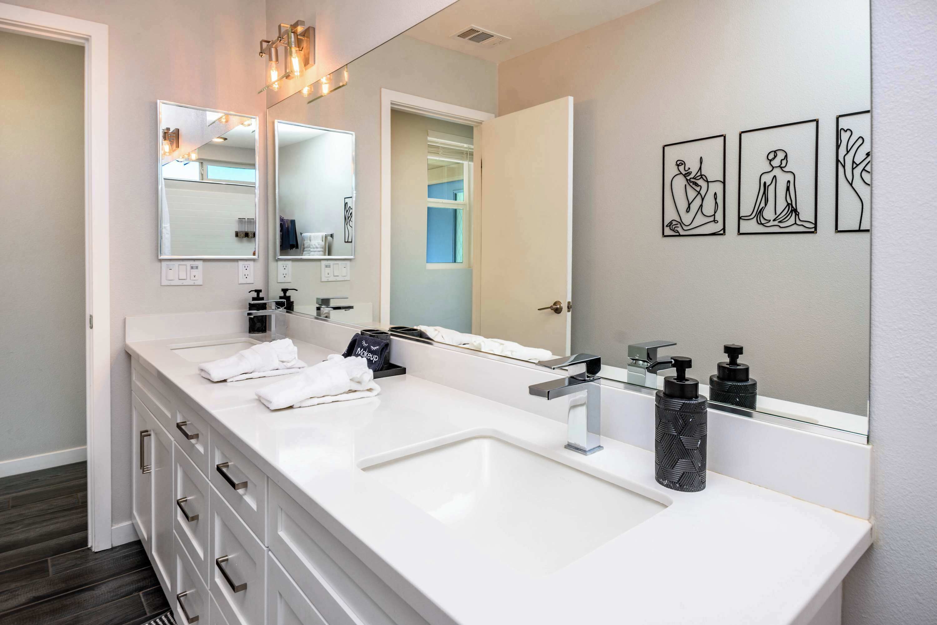 Un baño moderno con un tocador blanco, un espejo grande y tres obras de arte enmarcadas en la pared.