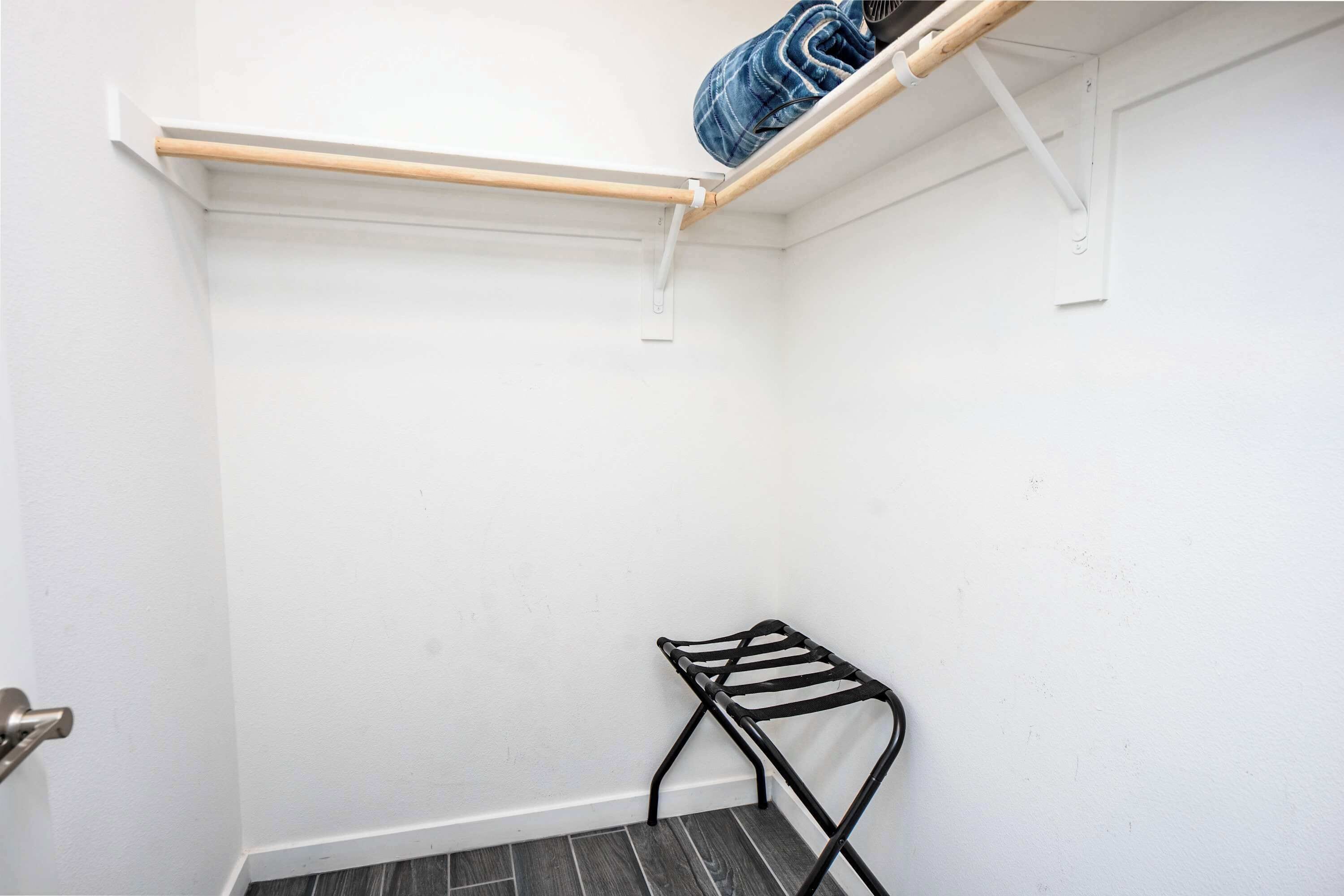 A small, white-walled room with a wooden shelf and a black metal rack.