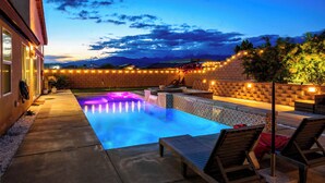 A swimming pool with lounge chairs and a brick wall with string lights.