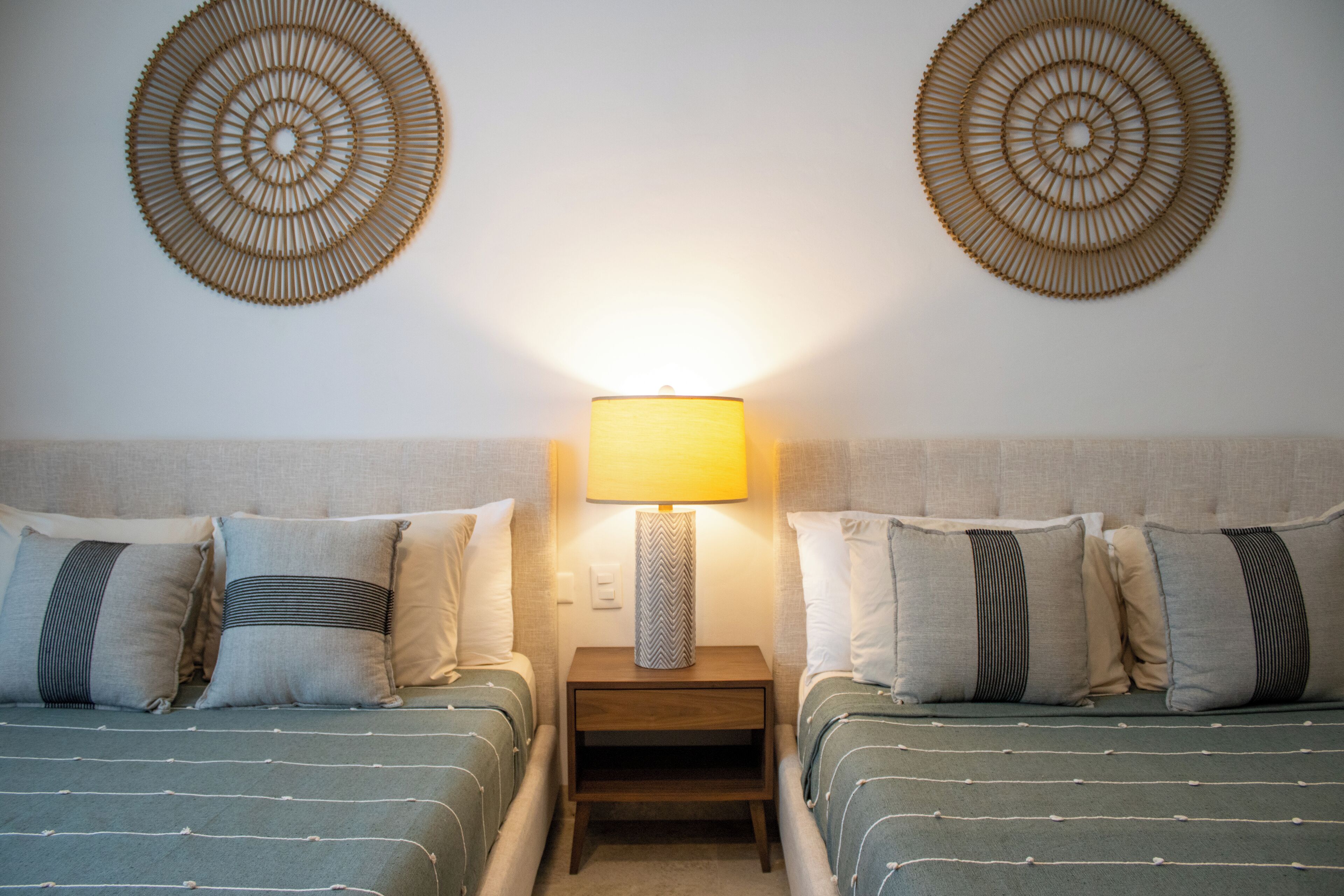 A hotel room with two beds, a nightstand with a lamp, and decorative wall art.