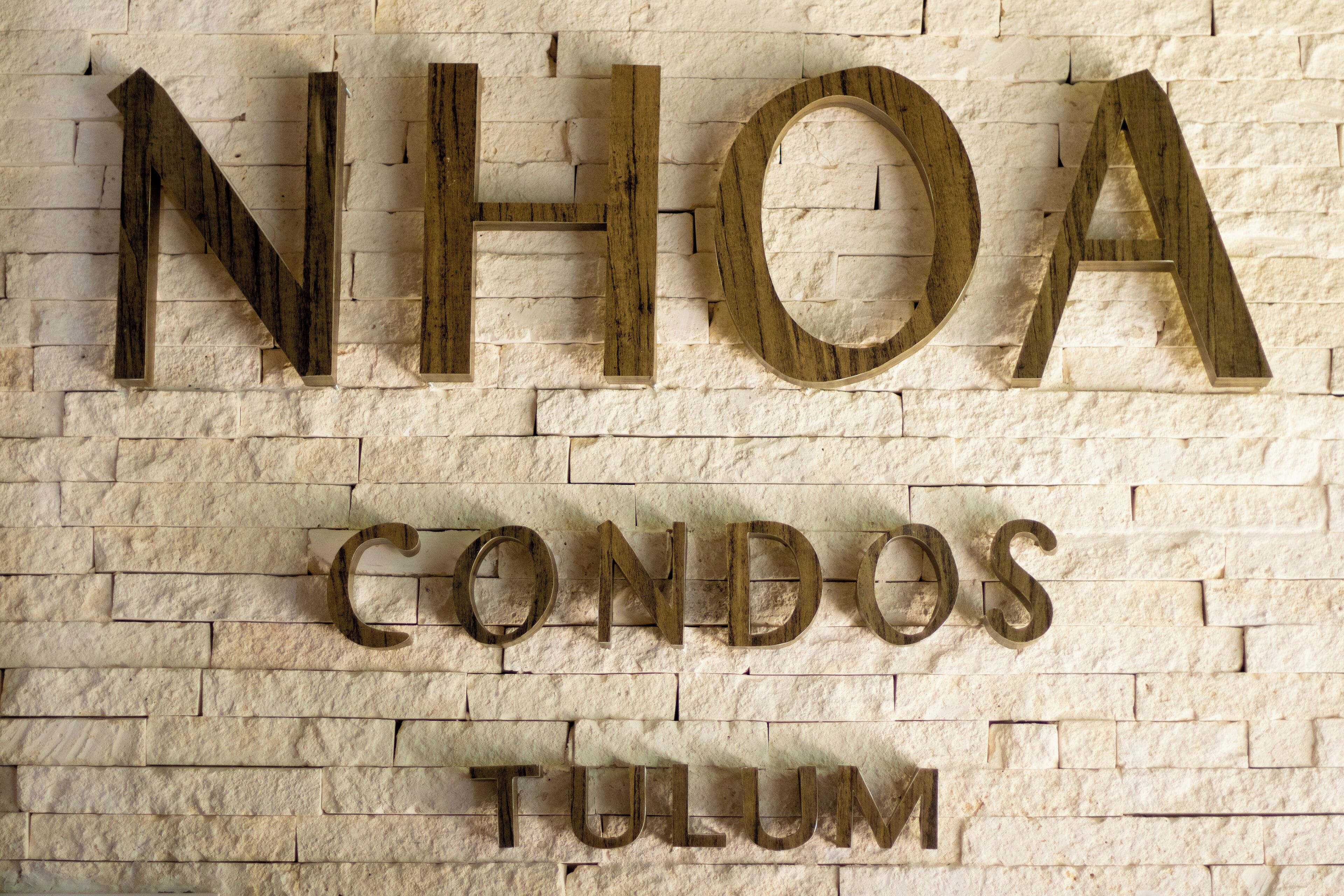 A sign with the text "NHOA CONDOS TULUM" on a brick wall.