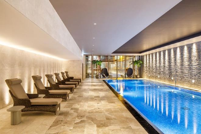 A long indoor swimming pool with lounge chairs along one side and a textured wall on the other.