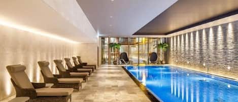 A long indoor swimming pool with lounge chairs along one side and a textured wall on the other.
