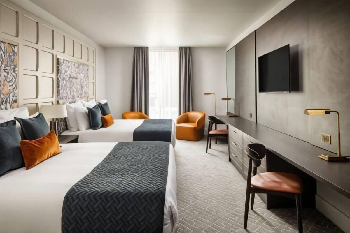 A hotel room with two beds, a desk, a chair, a TV, and a large window with curtains.