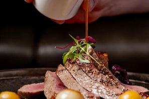 Gros plan d’un plat composé de viande coupée en tranches, de quelques accompagnements et d’une sauce versée dessus.