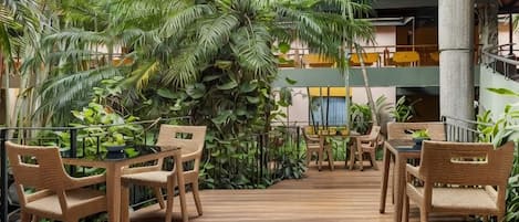 An outdoor seating area with wicker chairs and tables, surrounded by lush tropical plants.