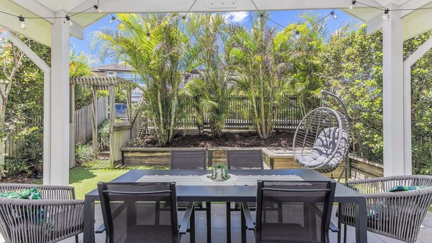 A covered patio with a table and chairs, surrounded by lush greenery and a hanging chair. - Dianella Dunes (Casuarina)