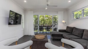 A modern living room with a grey sofa, white armchairs, a flat-screen TV, and a ceiling fan. - Dianella Dunes (Casuarina)