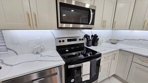 A modern kitchen with stainless steel appliances, white cabinetry, and marble countertops.