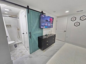 A modern bathroom with a teal sliding door, a black vanity with gold handles, and a mounted TV displaying a movie. - Funky Remodeled Otown Bungalow Sleeps 8 (Winter Park)