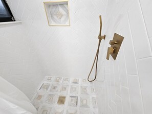A shower with a geometric tile pattern, a gold showerhead, and a small window with a diamond design. - Funky Remodeled Otown Bungalow Sleeps 8 (Winter Park)
