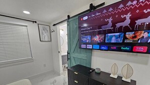 A modern living room with a large flat-screen TV mounted on the wall, a dark wooden cabinet with drawers, a green curtain, and a white sofa.