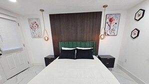 A bedroom with a large bed, two bedside tables, a wooden headboard, and wall-mounted artwork.