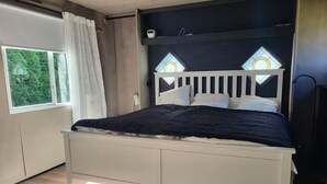 A bedroom with a bed, a window with curtains, and a view of greenery outside.